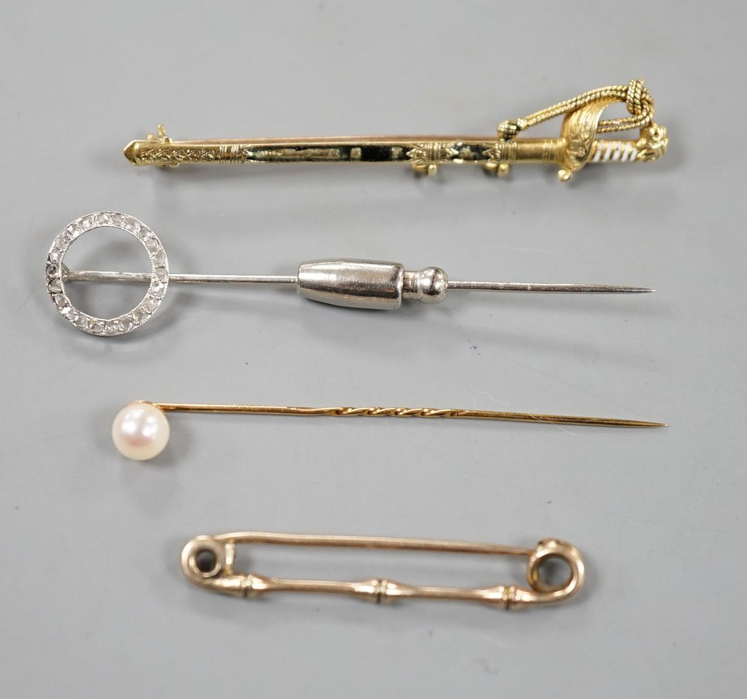 A French white metal (poincon mark for platinum) and diamond set tie pin, 64mm, gross 3.4 grams, a 15ct and enamel(a.f.) sword brooch, gross 4.7 grams and toe 9ct pins, one with cultured pearl, gross 3 grams.